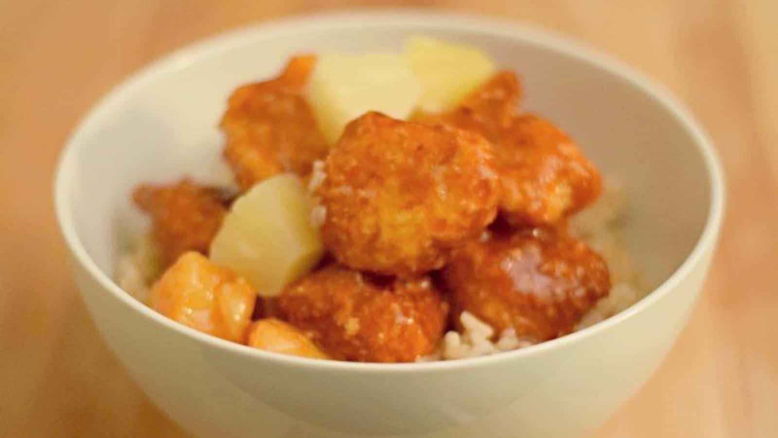 Image shows a Bowl of baked sweet and sour chicken with pineapple.