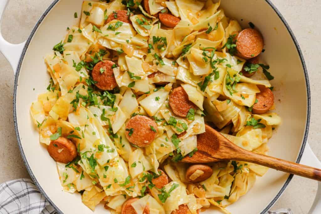 A pan of cabbage and sausage garnished with fresh herbs.