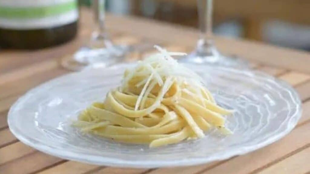 Image shows Cacio e Pepe on a plate with glasses in the background.