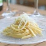 Image shows Cacio e Pepe on a plate with glasses in the background.