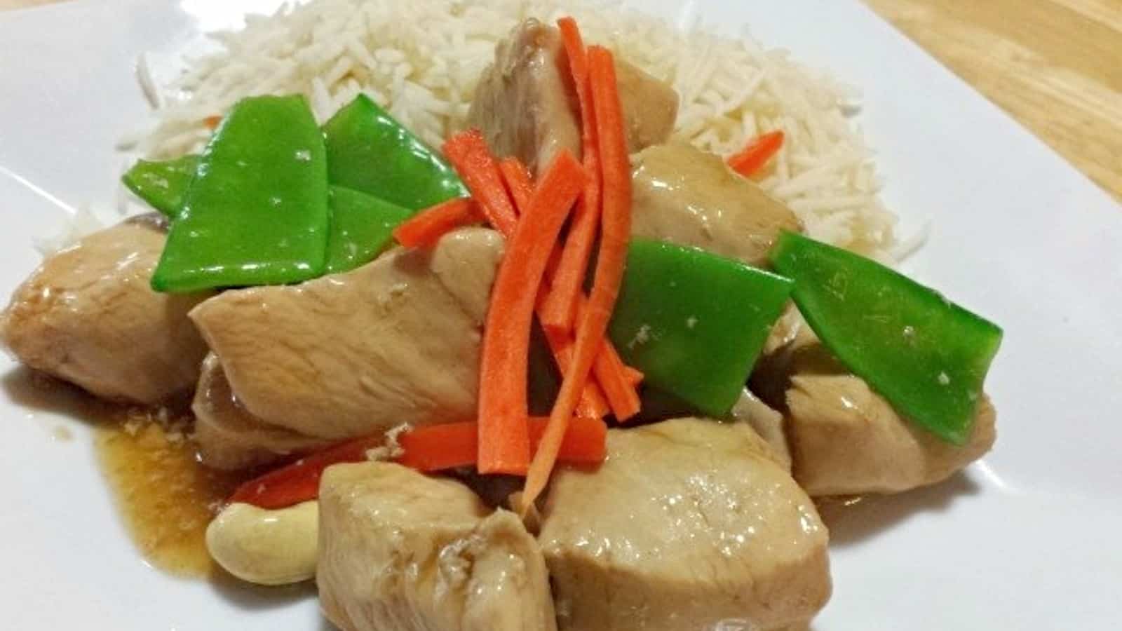 Image shows Cashew chicken on a white plate garnished with carrots and snow peas.