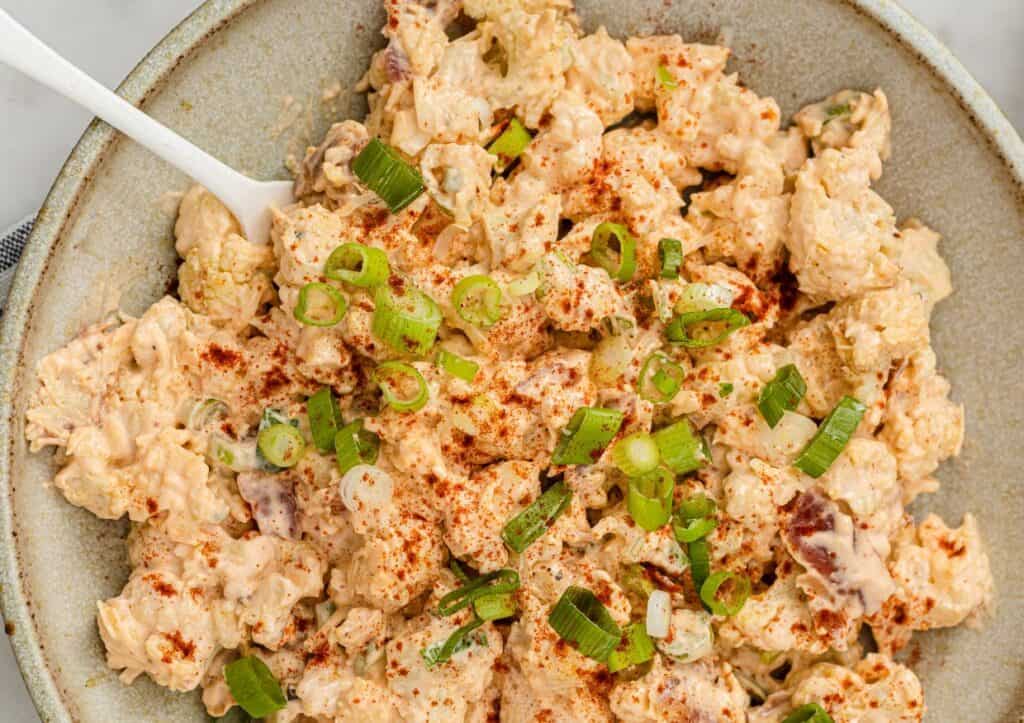 Cauliflower potato salad garnished with green onions with a fork.