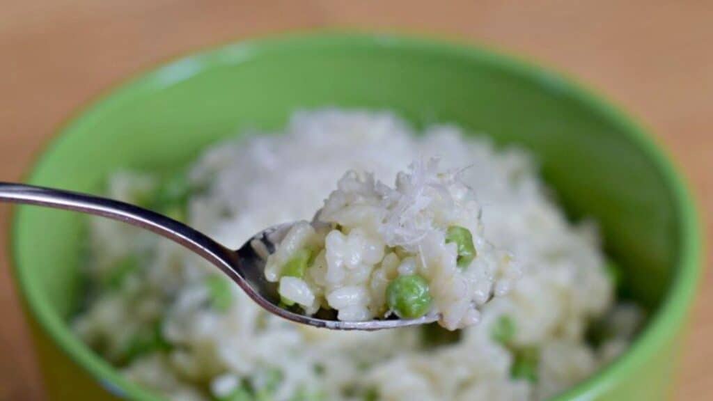 Image shows Chicken and pea risotto on a spoon with more in a green bowl behind it.