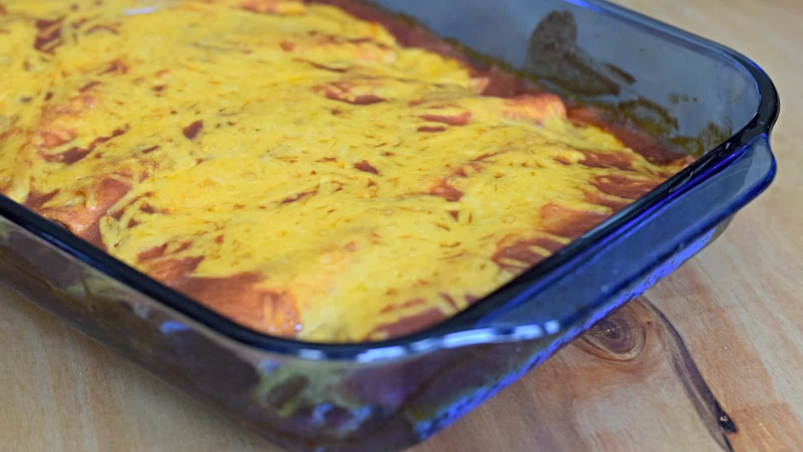 Image shows baked cheesy chicken enchiladas in a blue Pyrex casserole.