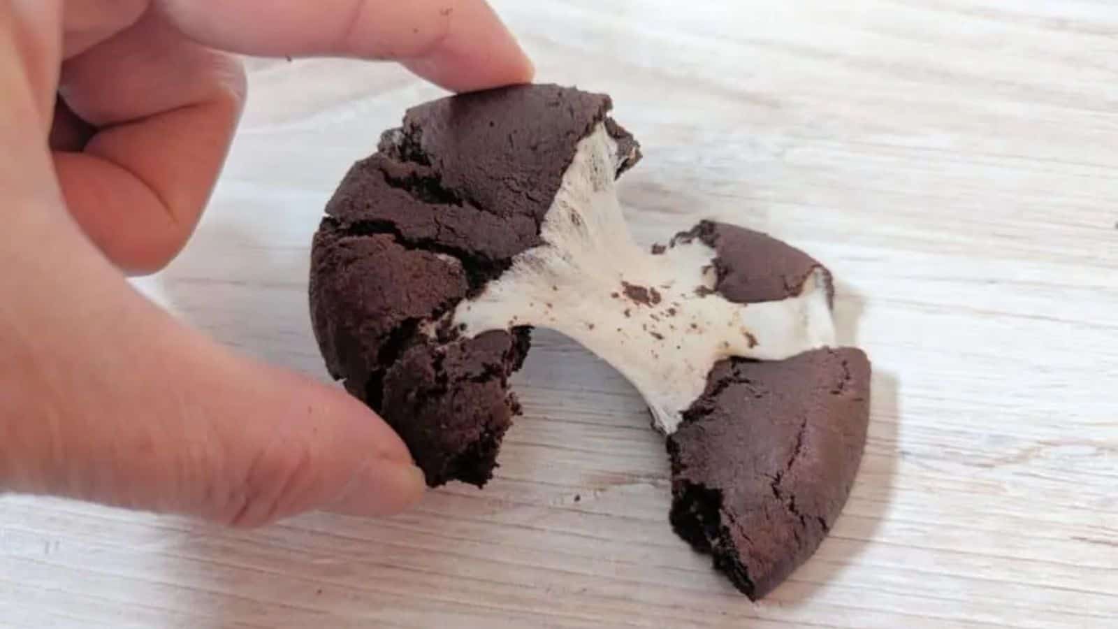 Image shows a Chocolate Marshmallow Cookie being pulled apart on a wooden table.