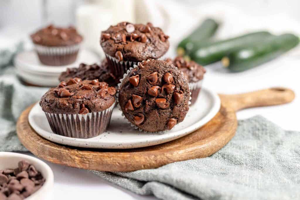 Chocolate Muffins on a plate on a cutting board with zucchini in the background.