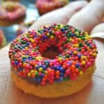 Image shows a Chocolate frosted mini donut held in a hand.