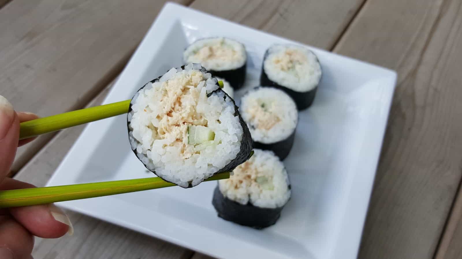 Image shows Chopsticks holding spicy tuna roll over a plate with more of the roll.