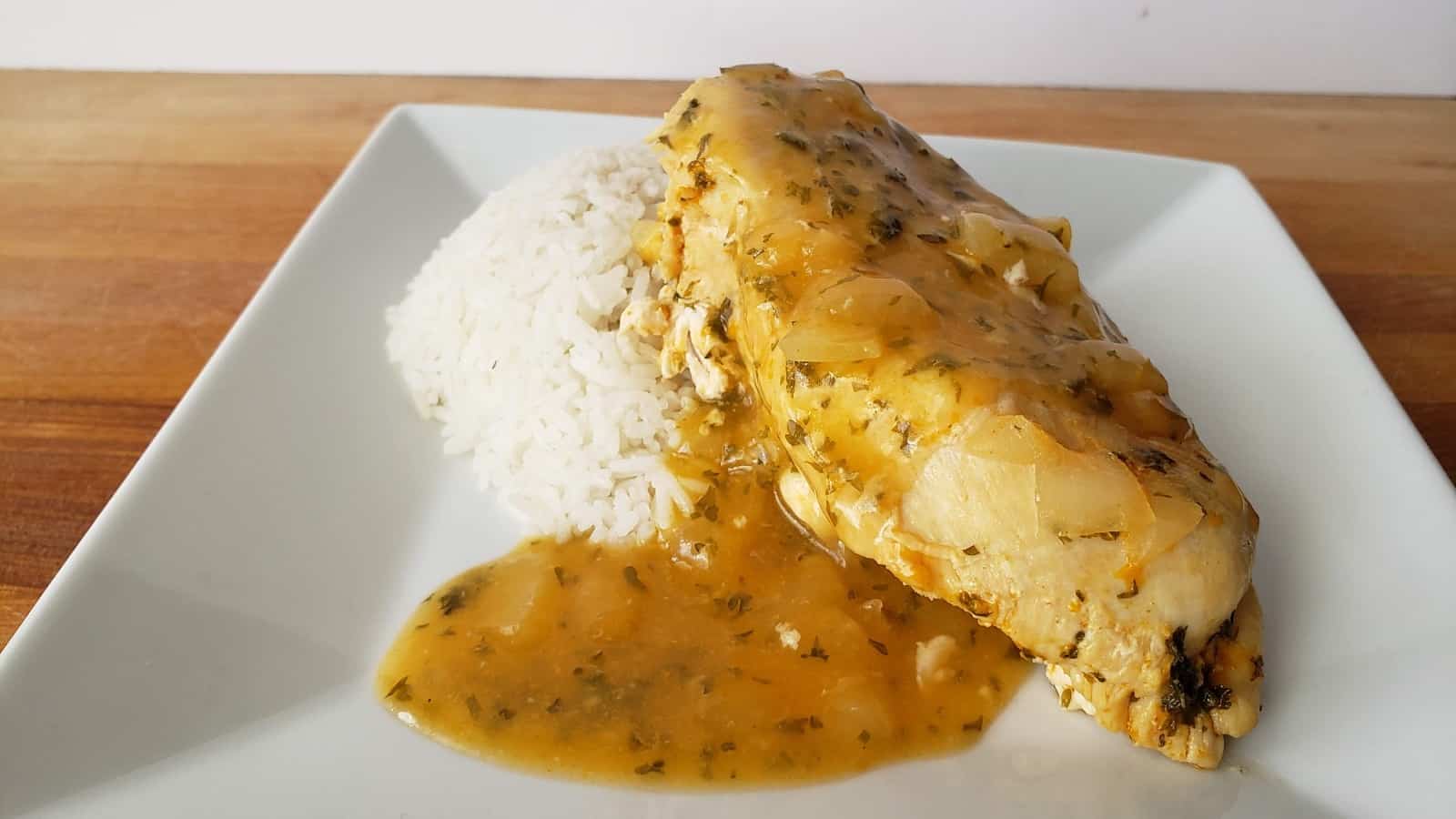 Close up image of lemon garlic chicken with rice on a white plate.