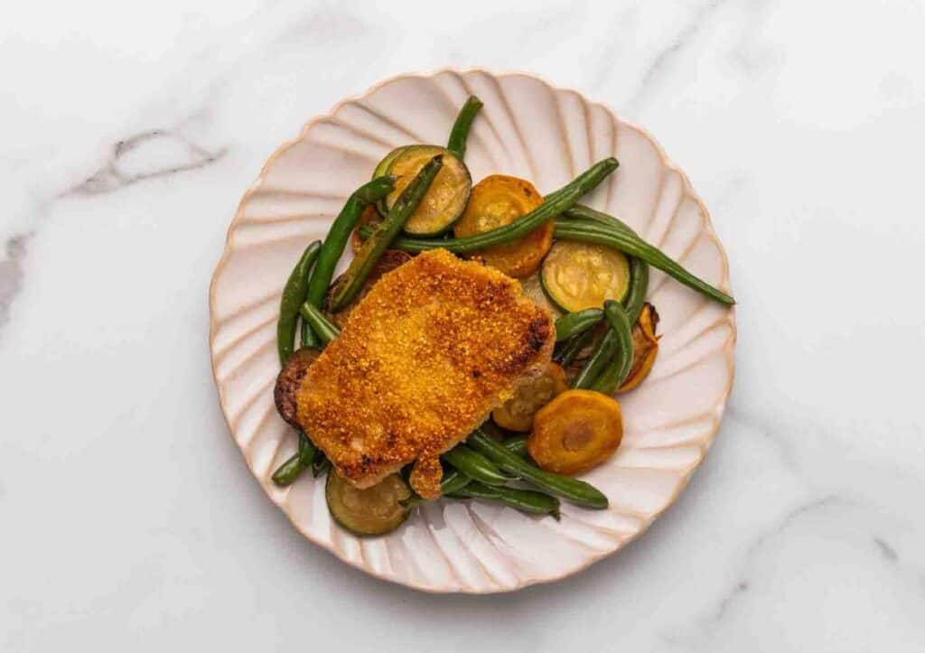 Pork chop over veggies on plate.