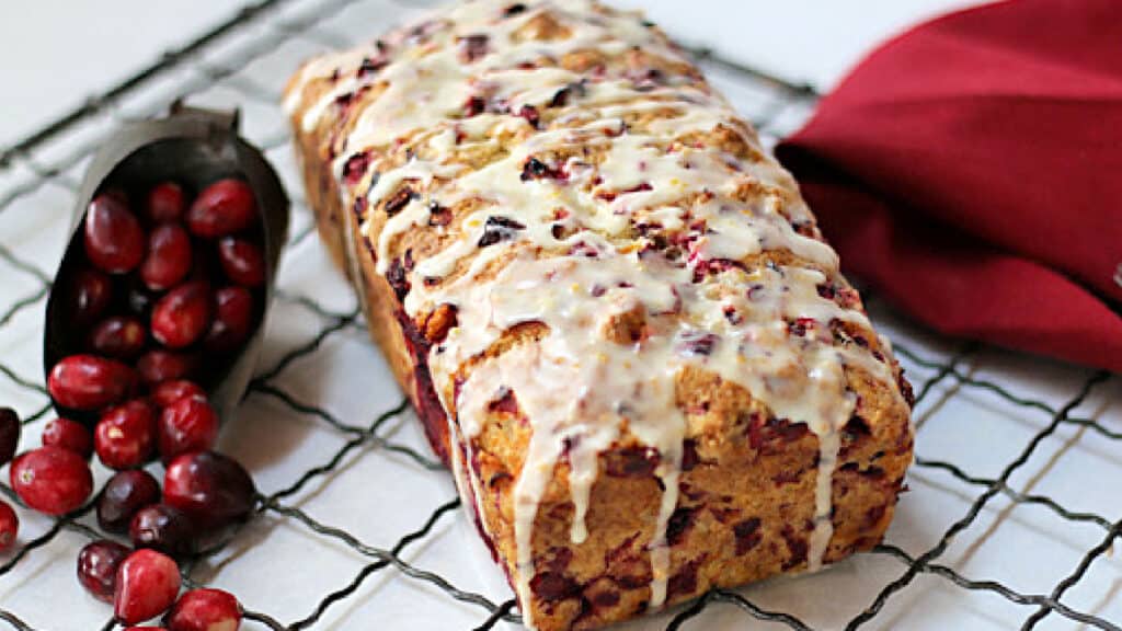 Cranberry bread on a wire rack with a red towel and fresh cranberries.