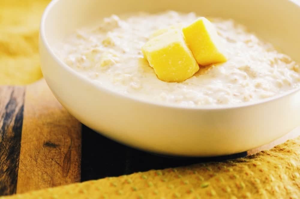 A large white ceramic bowl filled with creamy oats topped with fresh cubed mango.