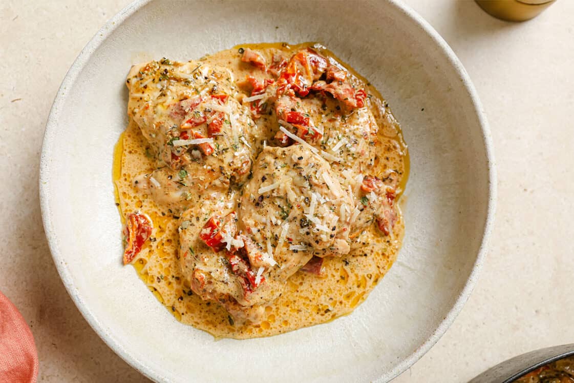 A skillet of creamy sun dried tomato chicken with a wooden spoon.