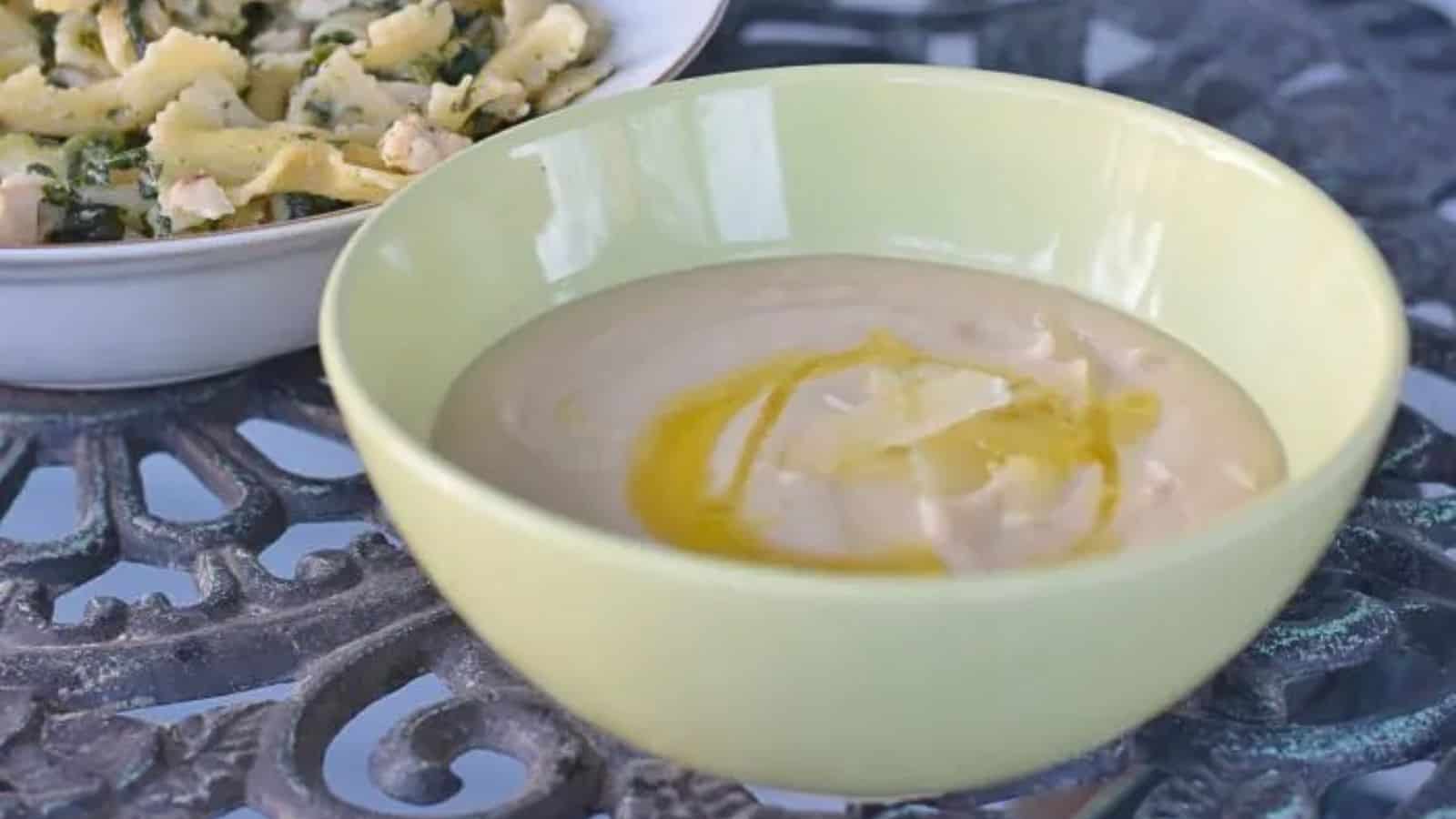Image shows a bowl of Creamy Tuscan Bean Soup with a drizzle of olive oil in a green bowl.