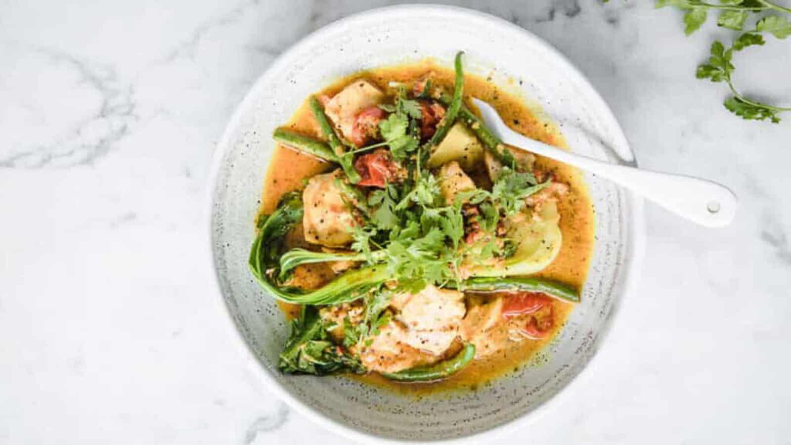 Curry salmon with coconut milk and bok choy in a bowl with a fork.