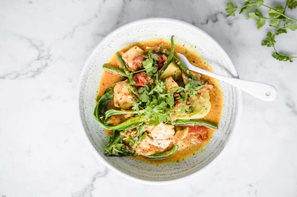 Curry salmon with coconut milk and bok choy in a bowl with a fork.