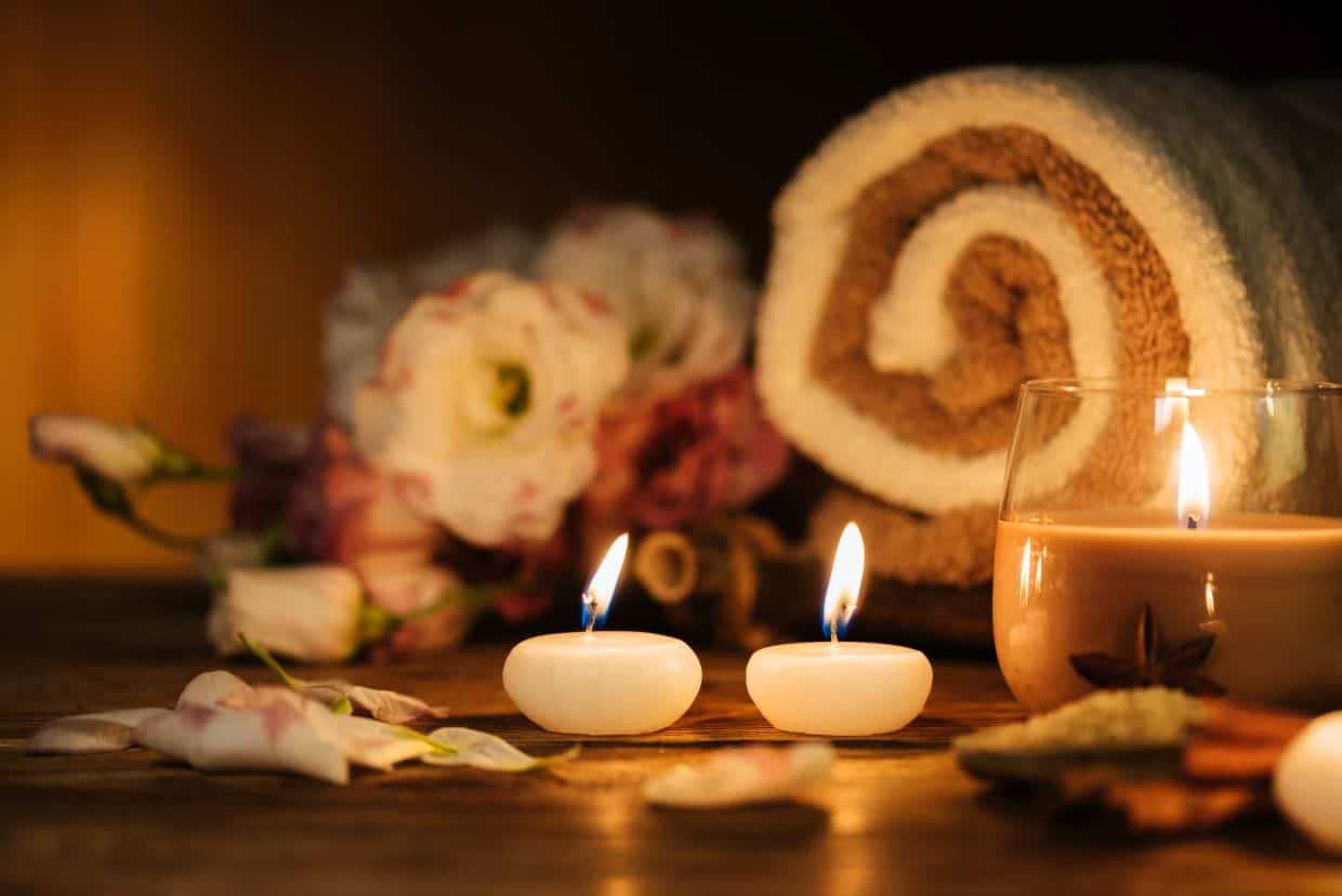 Three candles lit in front of flowers and a rolled towel.
