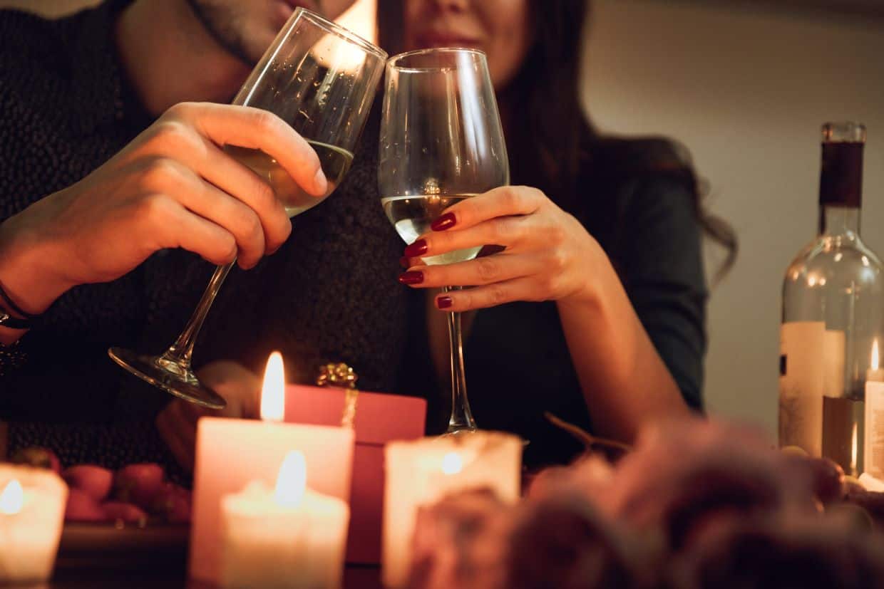 A couple holding two wine glasses behind lit candles.