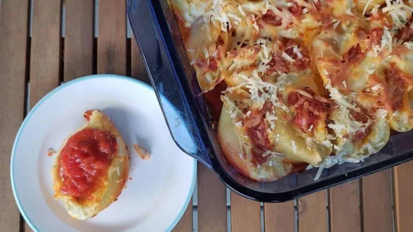 Image shows an overhead shot of Easy Cheesy Stuffed Shells with a small plate holding one and the rest of the pan next to it.