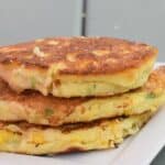 Image shows three corn fritters stacked atop each other on a white plate with a blue wooden background.