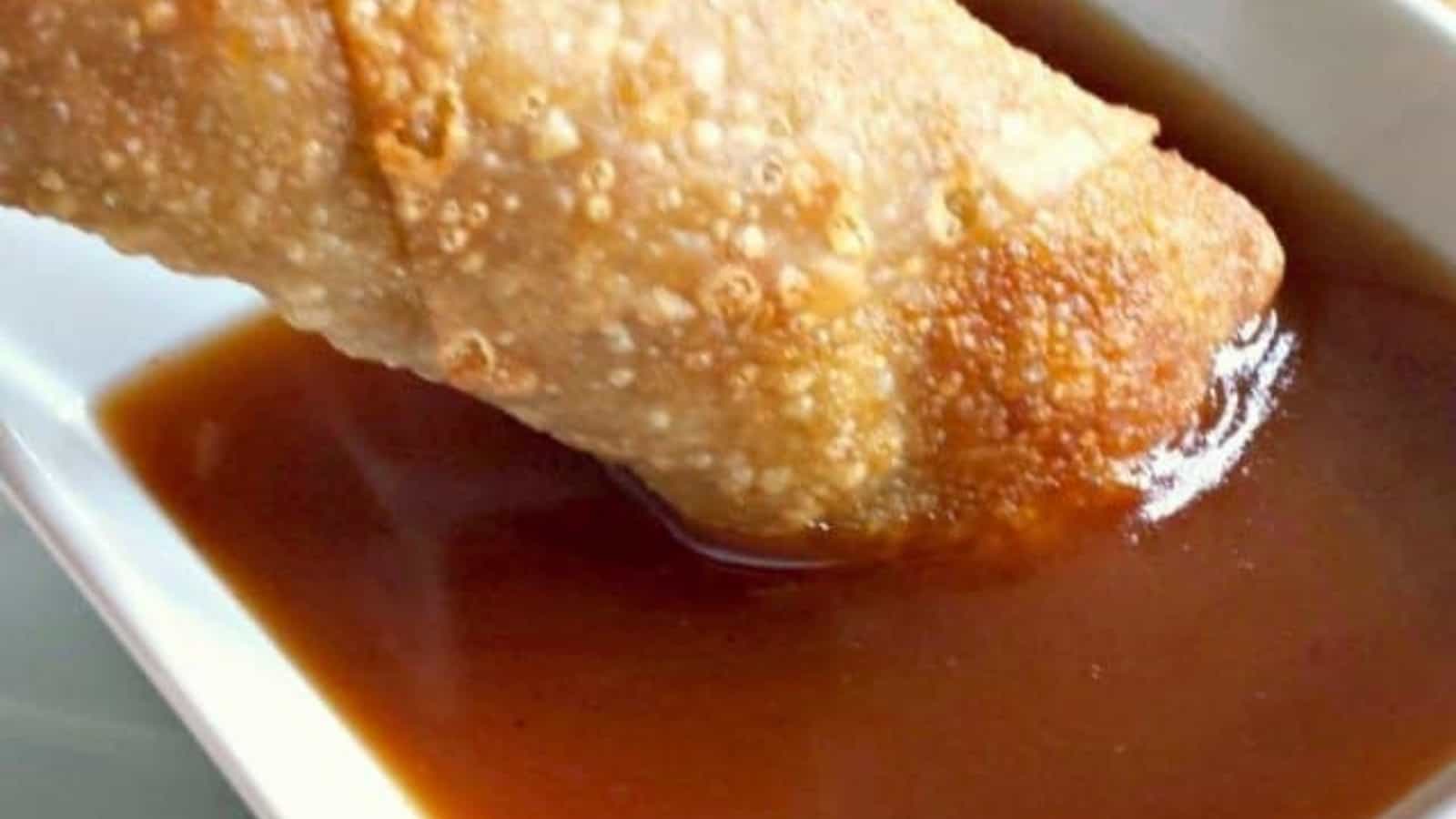 Image shows an Egg roll dipping into homemade sweet and sour sauce in a white bowl.