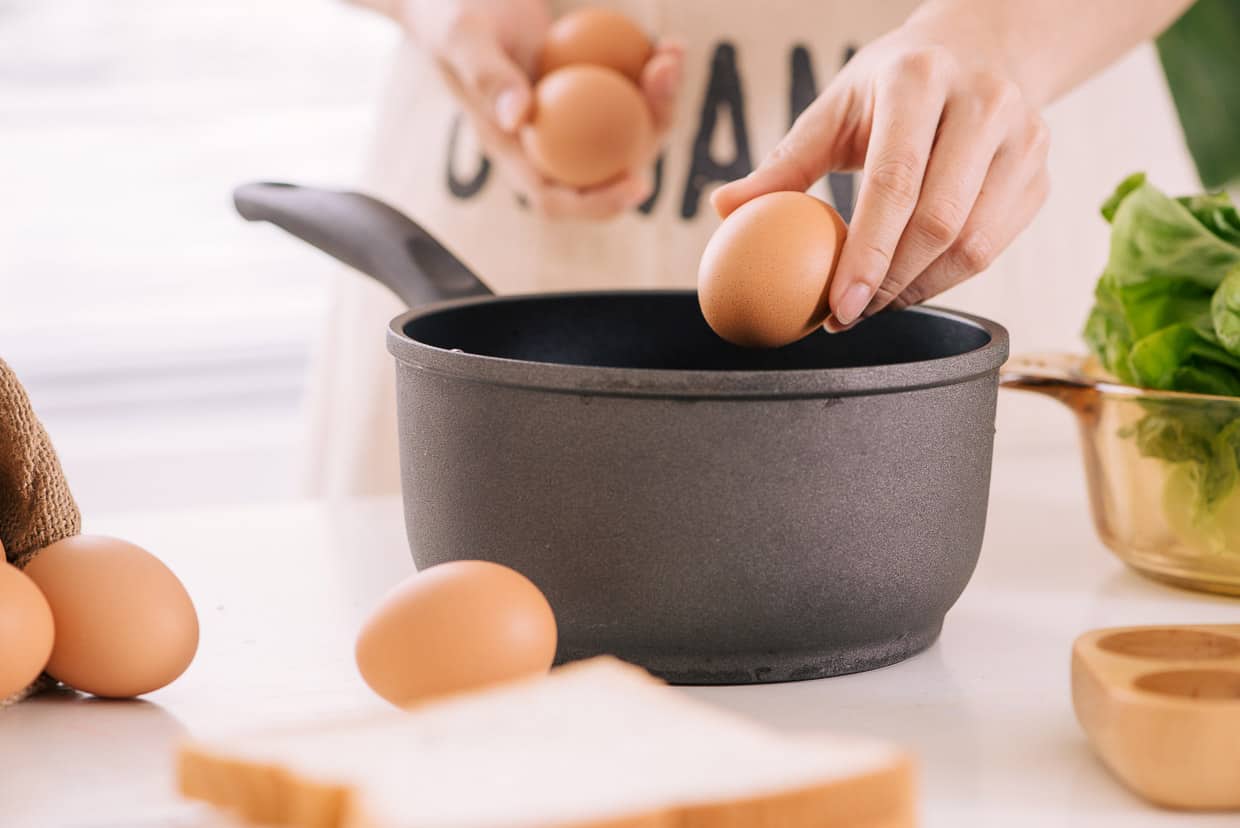 Someone putting eggs into a pan.