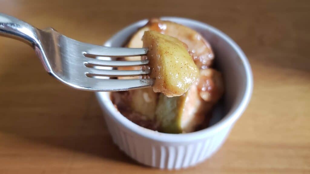 Image shows a Fork holding a bite of cinnamon apples with a ramekin holding more in the background.
