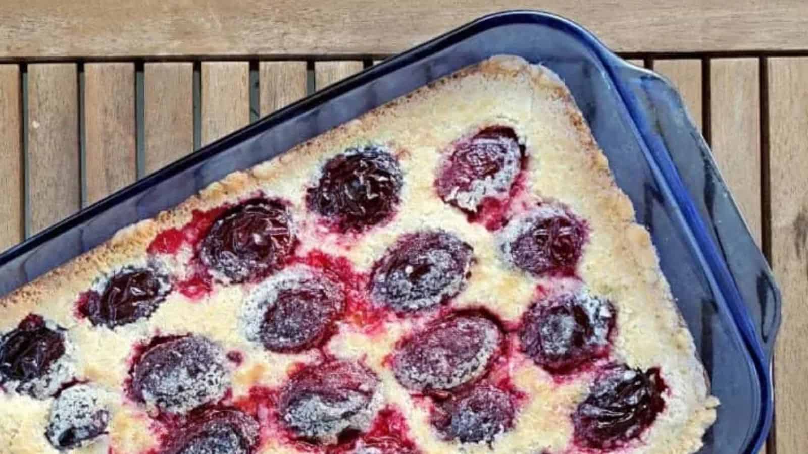 Image shows an overhead shot of German Plum Kuchen in a blue pyrex pan on a wooden table.