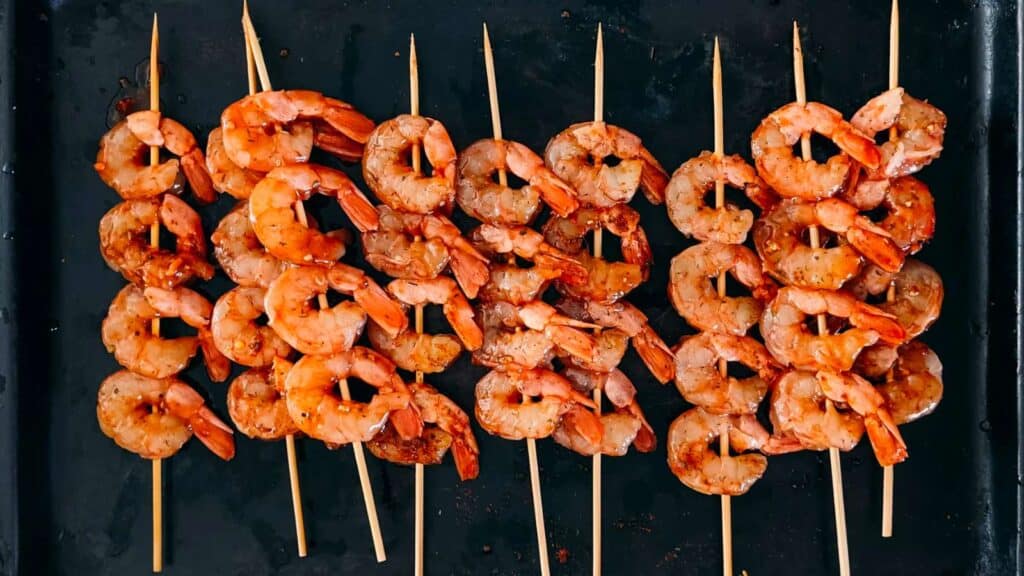 skewers of shrimp on a black pan.