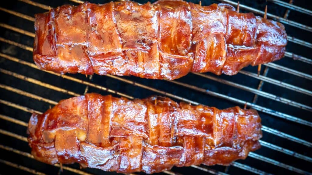 Two bacon-wrapped tenderloins on a smoker.