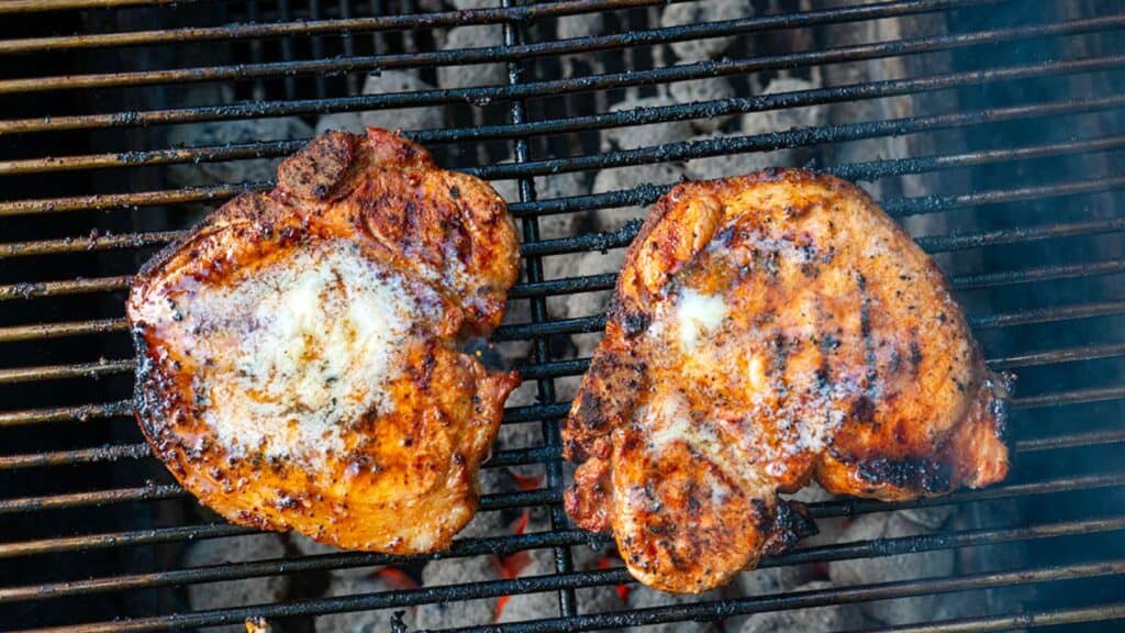 Two pork chops on grill with pats of butter.