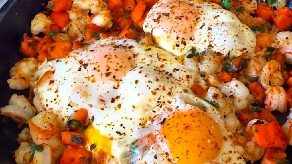 Pan of cooked eggs on shrimp hash.