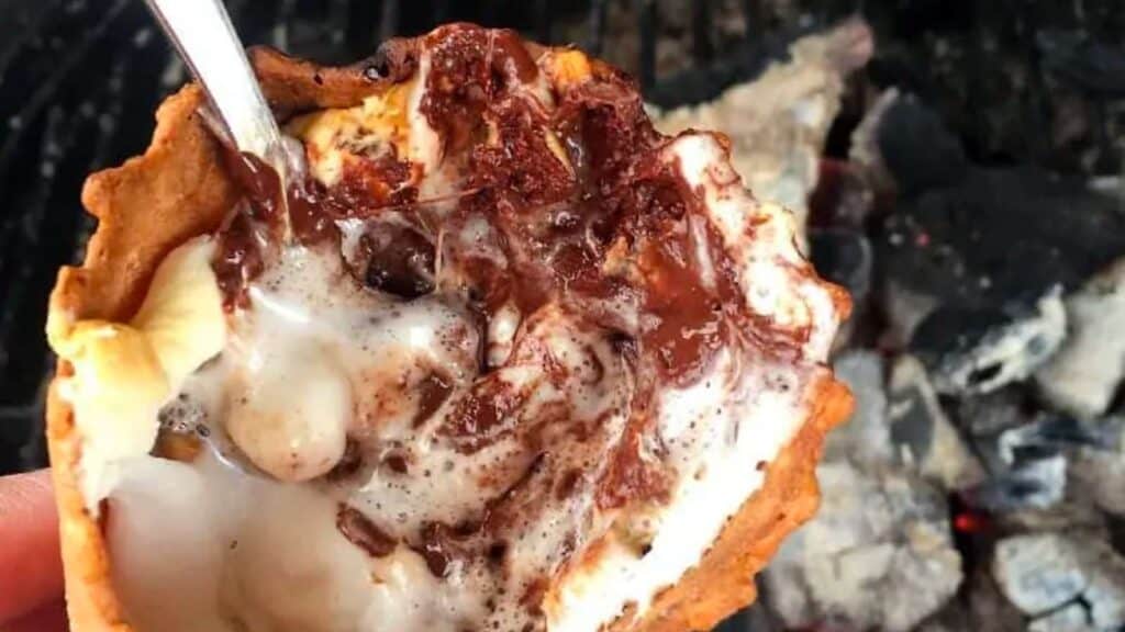 Melted marshmallows and chocolate in a waffle cone over a campfire.