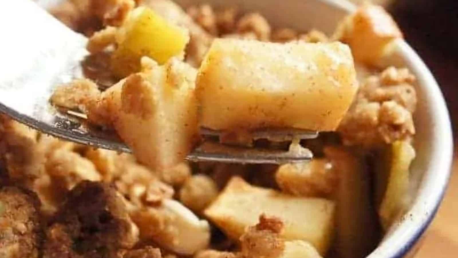 Image shows a close up of a fork holding a bite of Granola Apple Crisp with the whole serving behind it.
