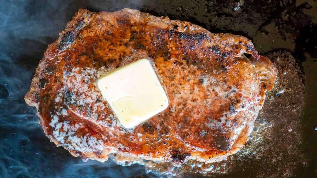 Ribeye steak searing on griddle with butter.