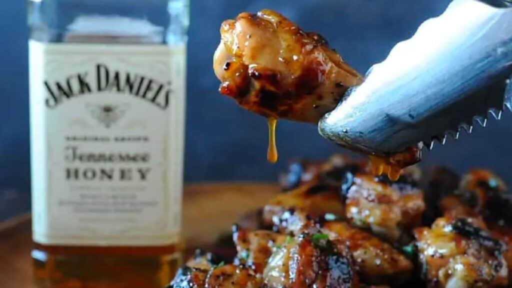 Tongs holding chicken wing dripping in Tennessee whiskey sauce.