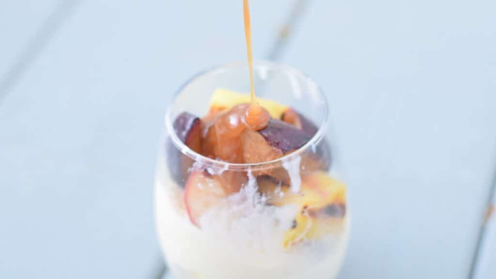 Grilled fruit with ice cream in a glass with caramel sauce being poured on it.