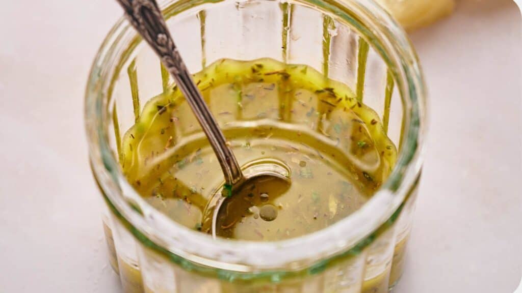 A jar with Italian dressing with it and a teaspoon resting in it.