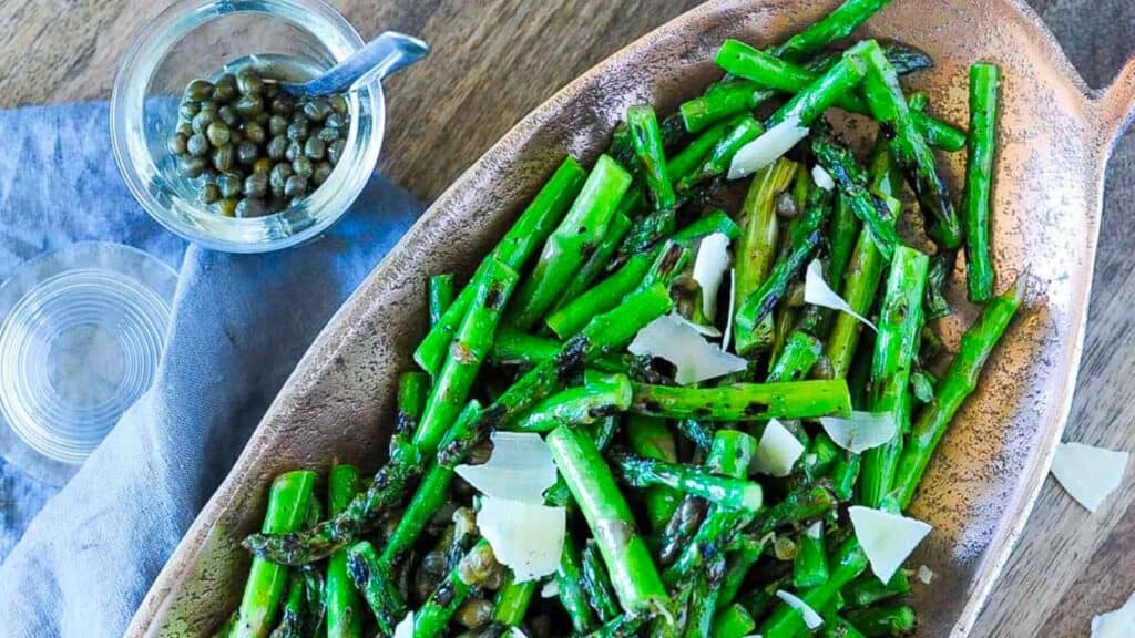 Bowl of grilled asparagus with parmesan and capers.