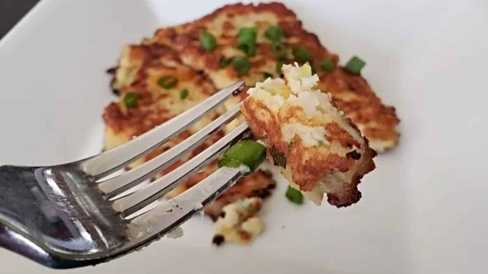 Image shows Loaded Mashed Potato Pancakes on a fork with the full piece on a white plate behind it.