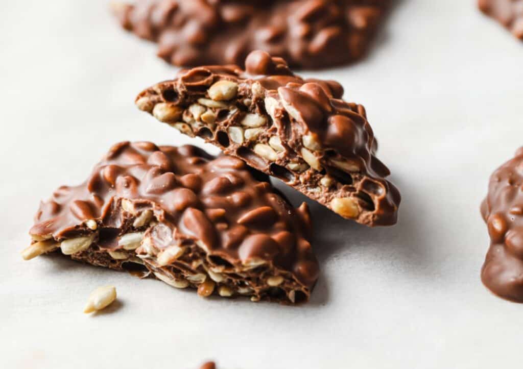 Two halves of a low-carb milk chocolate sunflower seed cluster stacked on top of each other.