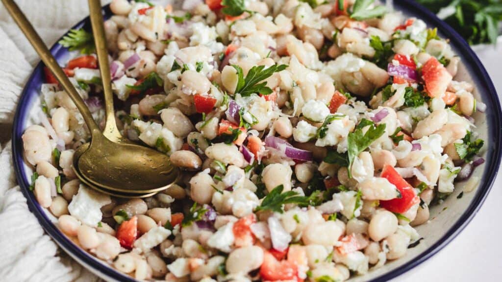 side view of white bean salad in bowl with tongs.