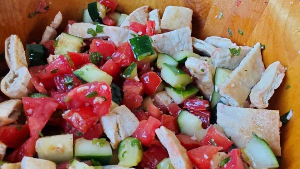 Image shows a close up shot of Mediterranean pita salad in a wooden bowl.