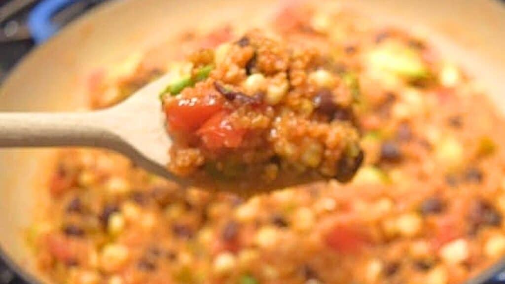 Image shows a wooden spoon holding some Mexican Skillet Quinoa over a pan containing the remainder of the dish.