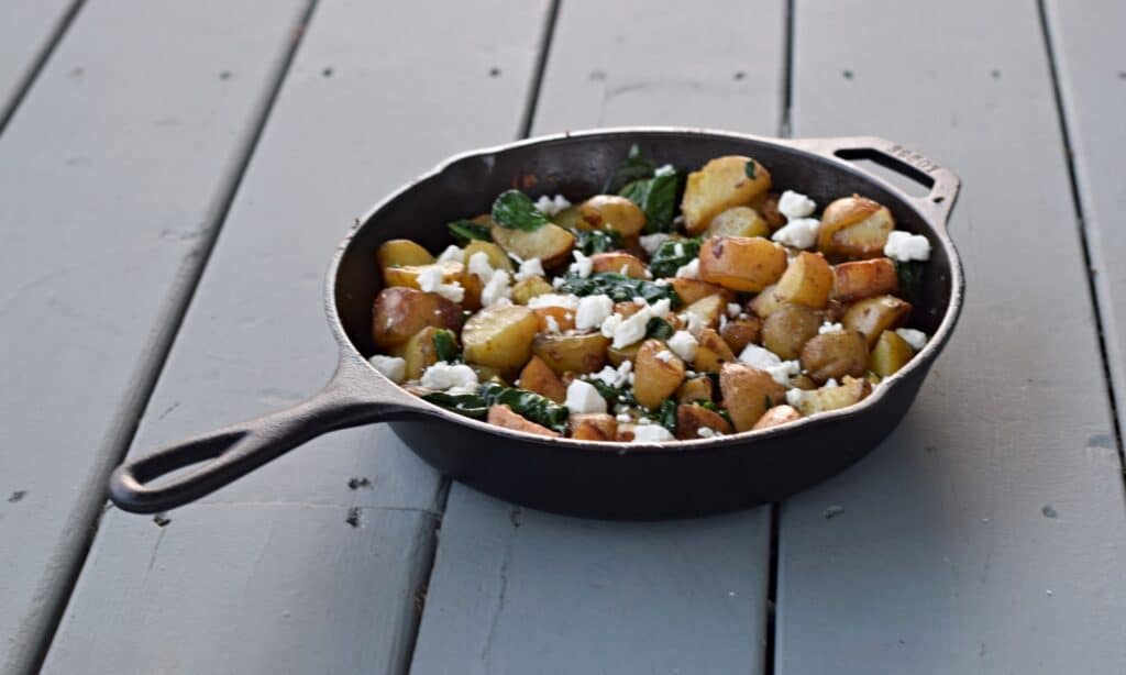 Oven roasted potatoes with spinach and goat cheese in a cast iron pot.