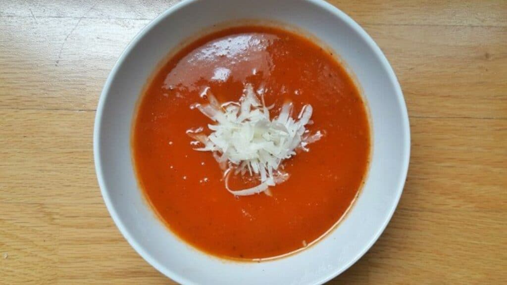 Overhead image of a bowl of tomato soup with parmesan grated into it.