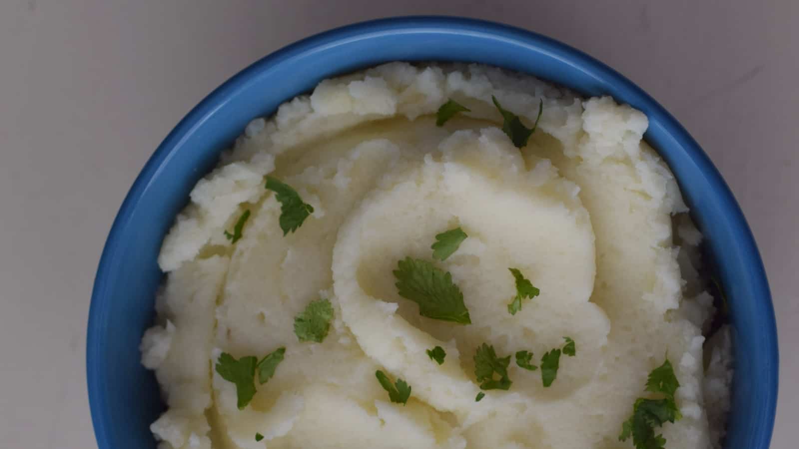 Overhead shot of a bowl of mashed potatoes in a blue bowl with parsley sprinkled over it.