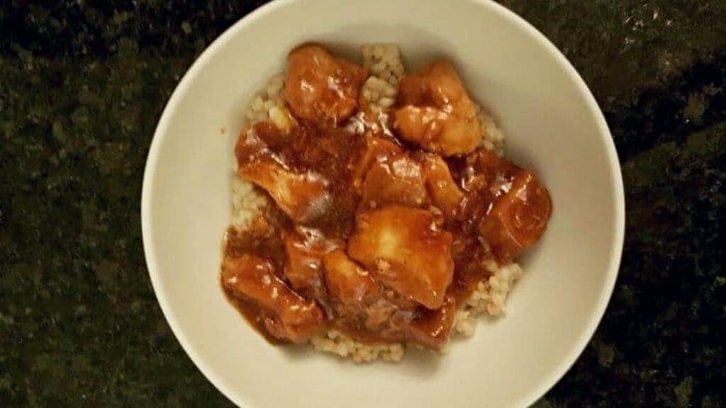 Overhead shot of honey bourbon chicken in a bowl on a black counter.