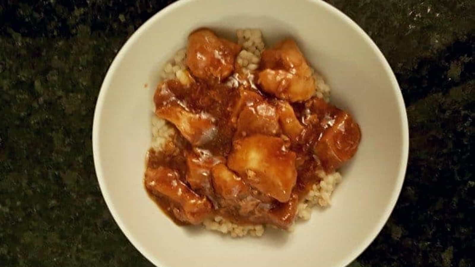 Overhead shot of honey bourbon chicken in a bowl on a black counter.