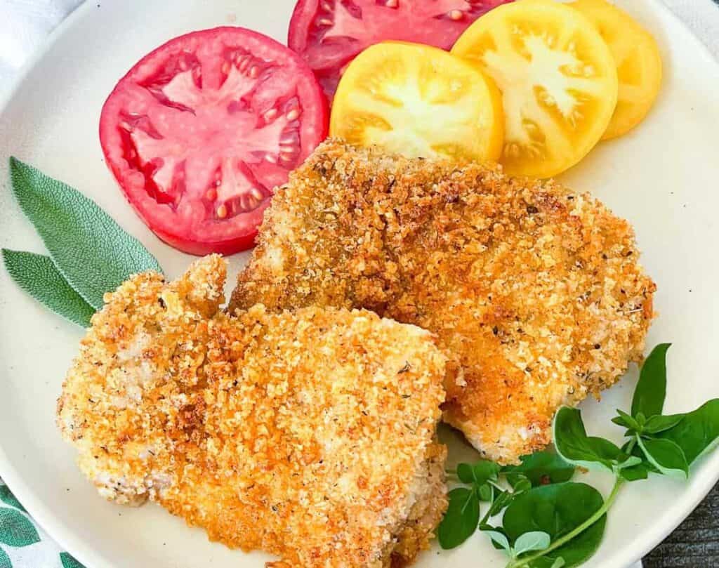Panko coated chicken on a plate with sliced tomatoes.